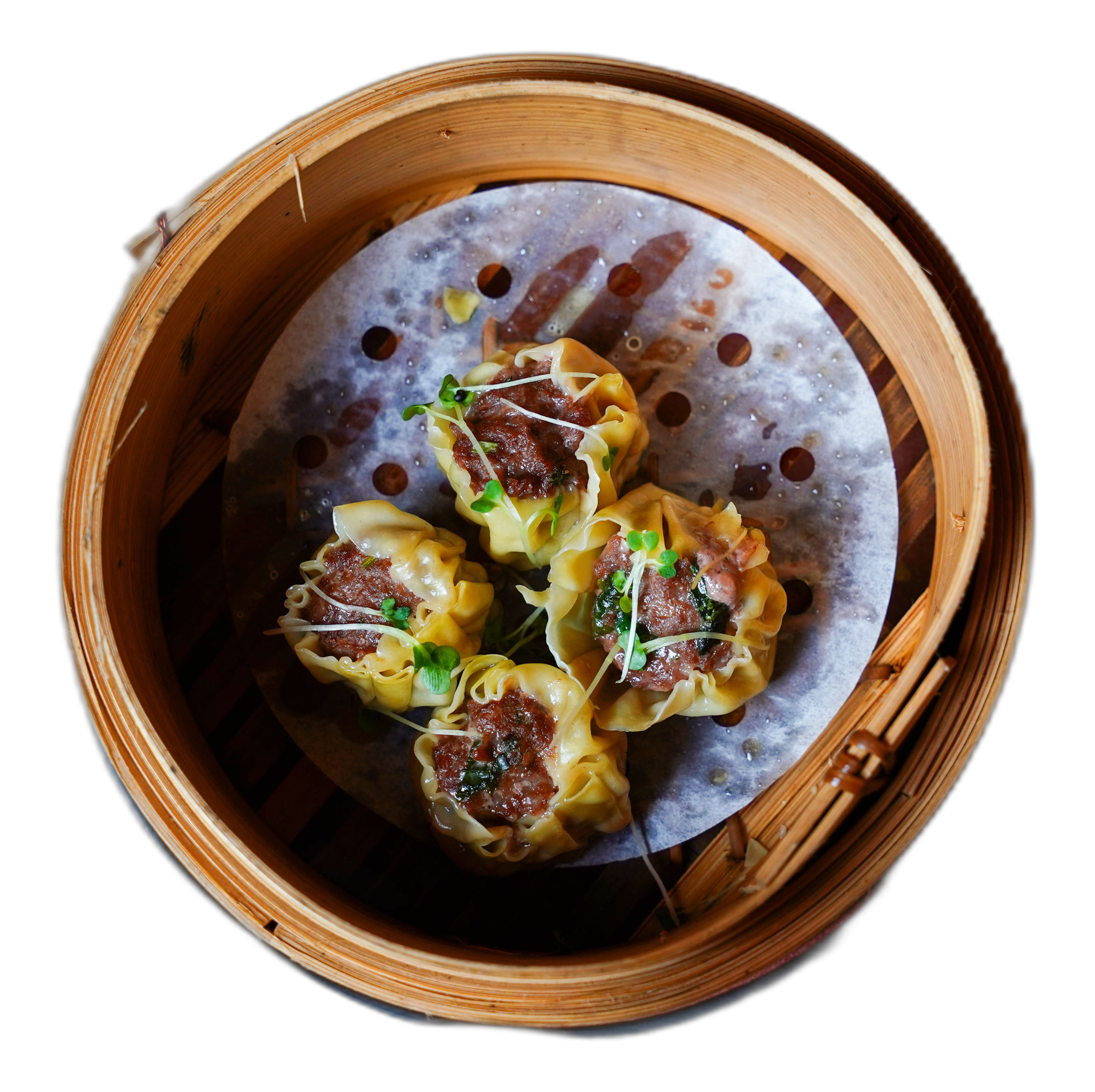 Steamed dumplings in a bamboo basket, garnished with greens, set on a dark background.