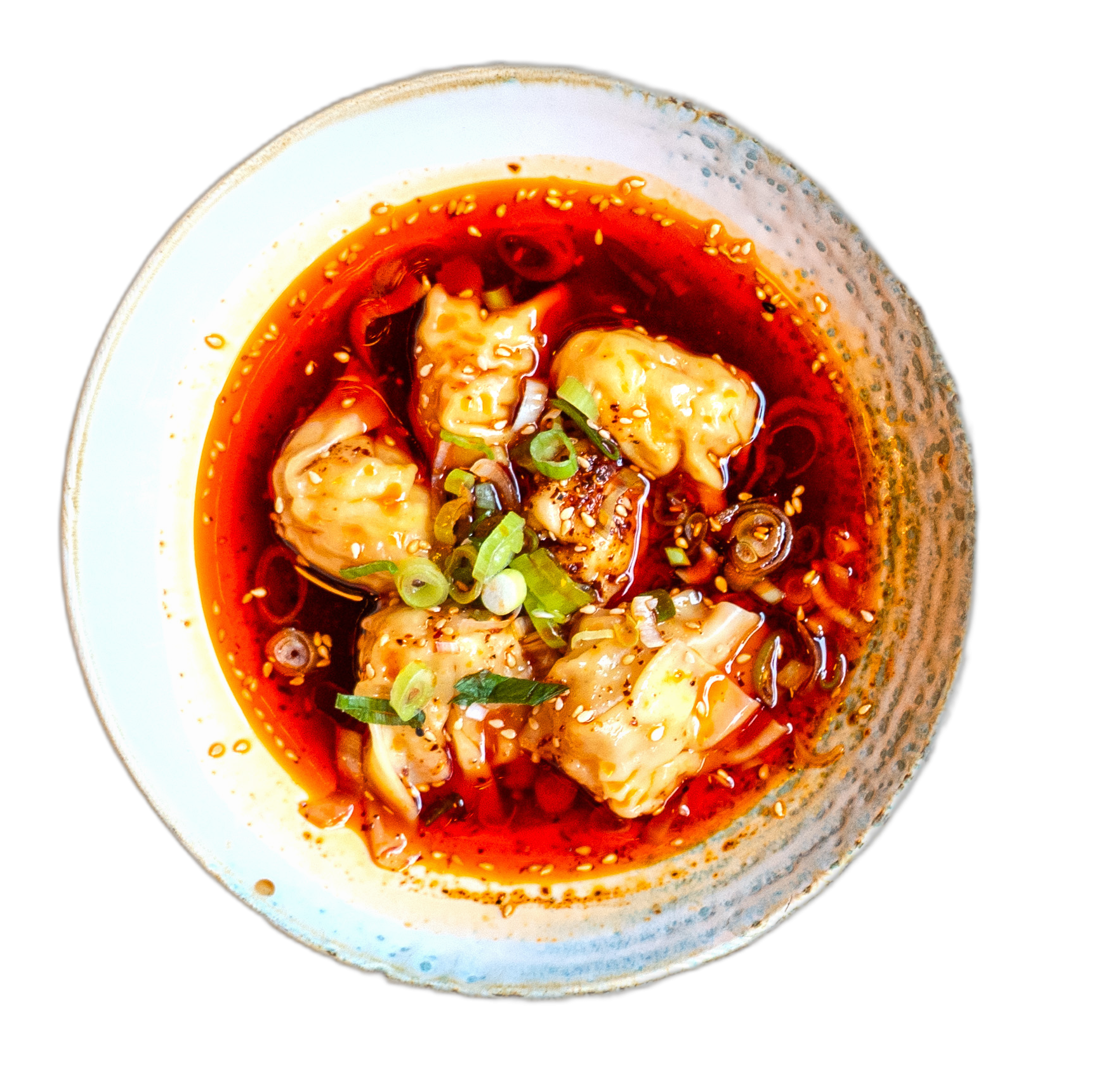 Top-down view of a bowl with dumplings in red chili oil, sprinkled sesame seeds and chopped scallions.